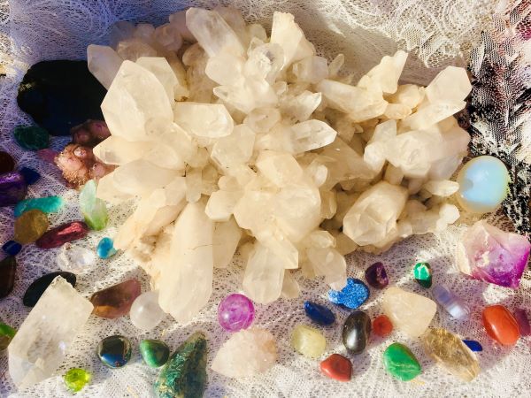 A clear quartz crystal cluster with multi-coloured semi-precious stones surrounding the clusterco